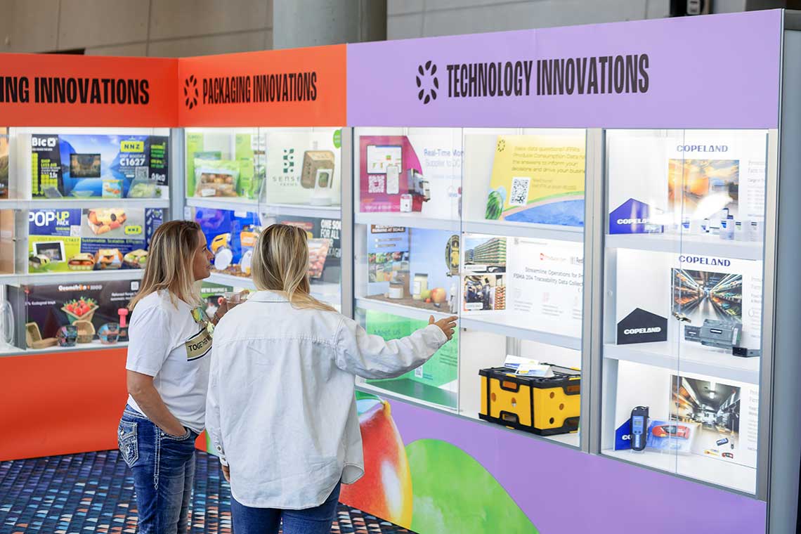 Two women examining a display case at an exhibition showcasing packaging and technology innovations.