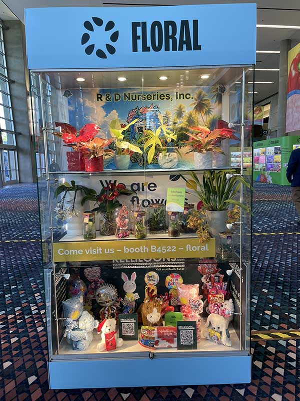 Display case labeled "FLORAL" with plants and decorative items in a convention hall.