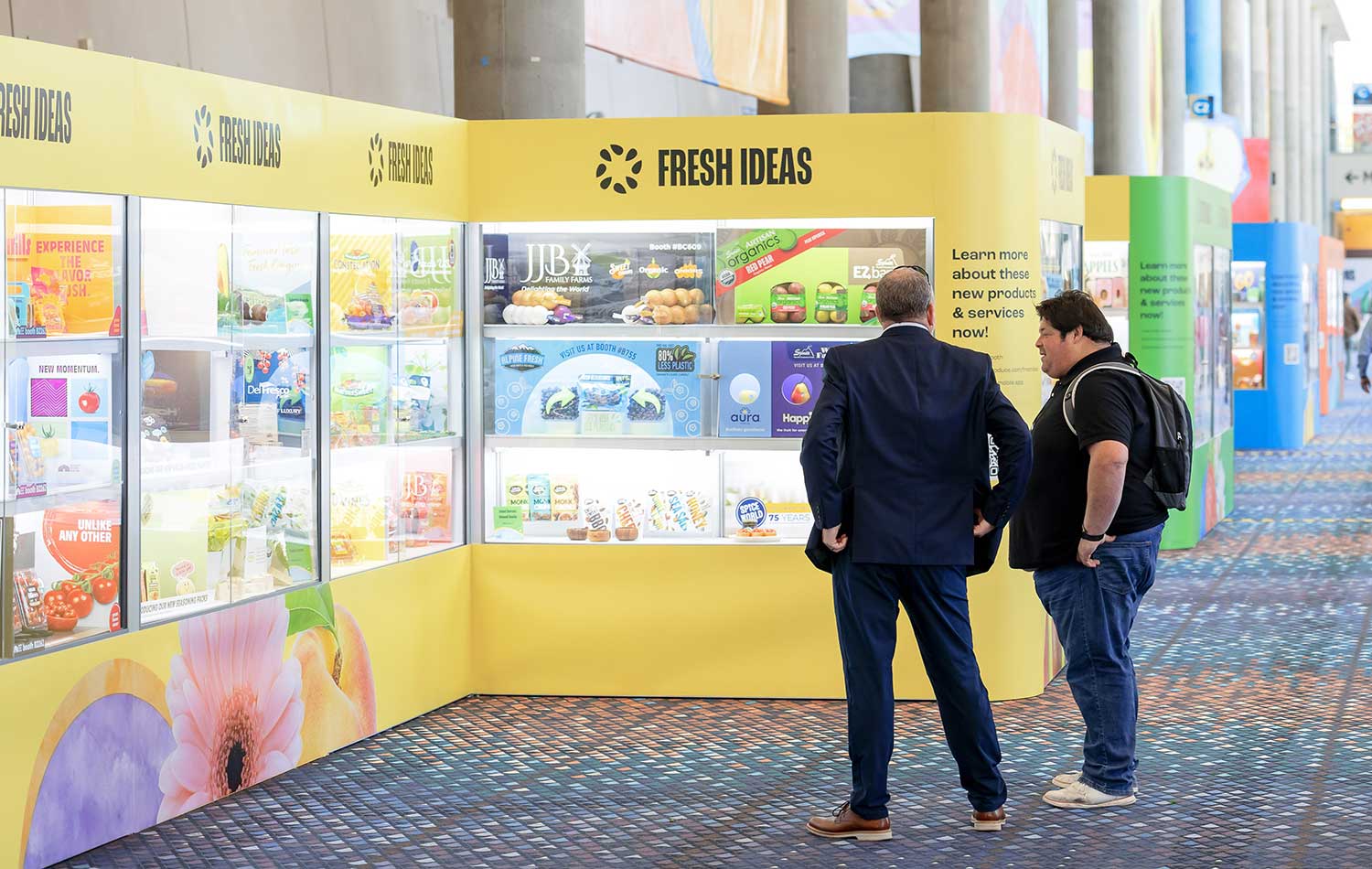 Two men looking at a "FRESH IDEAS" booth displaying food products.