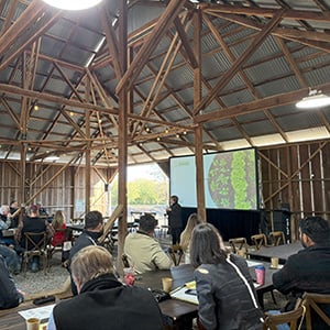 People attending a conference in a wooden barn with a presentation in progress.